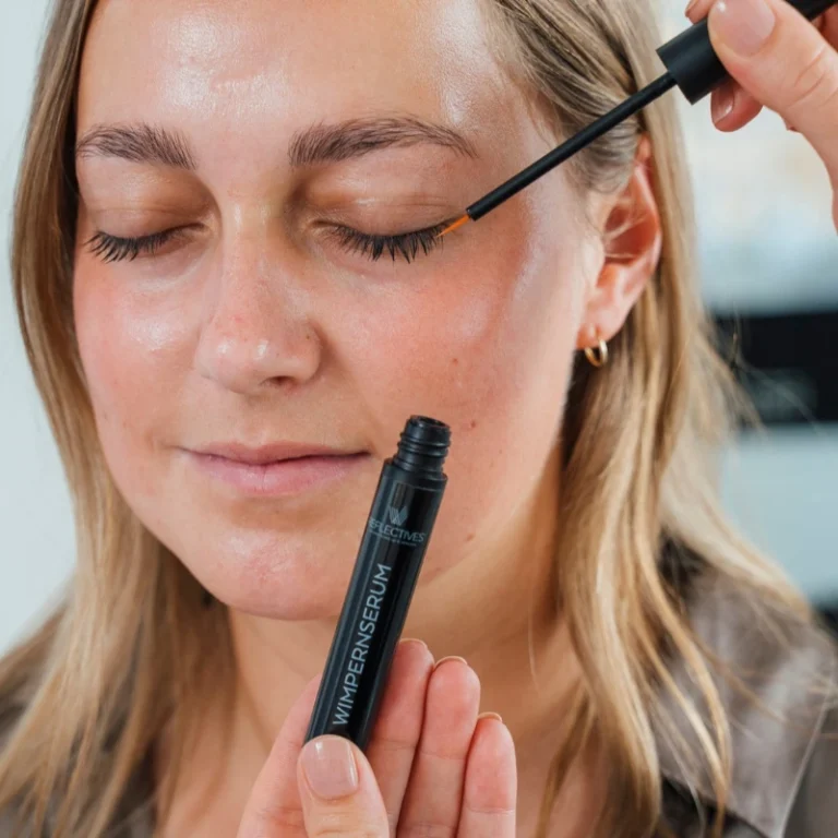 Einem Model mit langen Wimpern und dichten Augenbrauen wird das REFLECTIVES Wimpernserum aufgetragen.