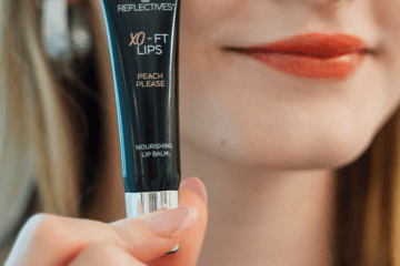 Frau hält getönten Lip Balm (Lippenpflege) in der Hand, um die auf ihren Lippen aufgetragene Farbe zu demonstrieren.